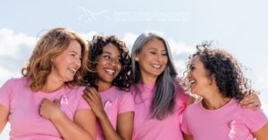 Four women hugging and smiling, wearing pink t-shirts in support of Breast Cancer Awareness